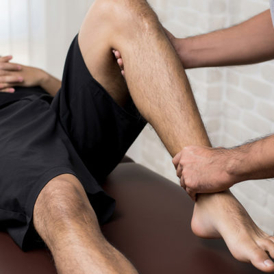Therapist treating injured leg of athlete male patient in clinic - sport physical therapy concept