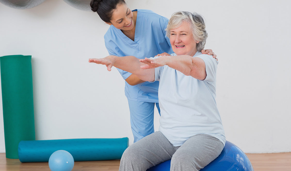 Happy instructor assisting senior woman in exercising at gym